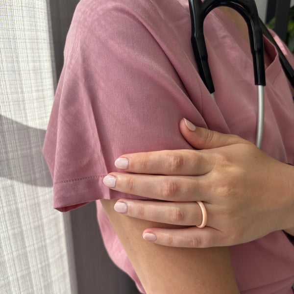 Person wearing a pink shirt with a stethoscope around their neck, and posing to show a pink silicone ring.